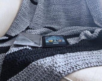 Könnte beinhalten: Eine graue und schwarze gestreifte gehäkelte Wolldecke, die über ein Sofa gelegt ist. Die Decke hat ein dezentes, strukturiertes Muster.
