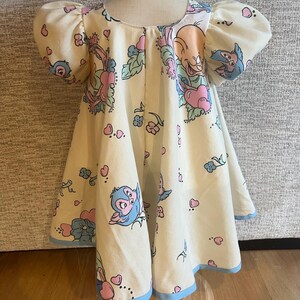 May include: A cream-coloured dress with a blue trim. The dress has a cartoon print of birds and hearts.