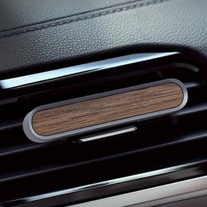 Peut inclure: Support de téléphone pour grille d'aération de voiture avec un design rectangulaire en bois. Le support a un cadre argenté et est placé contre un tableau de bord de voiture noir. La section en bois a un grain de bois naturel.