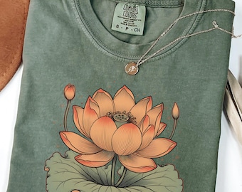 May include: A green t-shirt with a vintage-style illustration of a lotus flower in orange and yellow. The shirt has the text "COMFORT COLORS" on the tag.