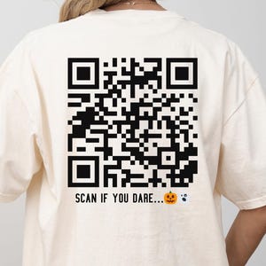 May include: Ivory-colored t-shirt with a large black QR code graphic on the back. The text "SCAN IF YOU DARE..." is printed below the code, along with a jack-o'-lantern and a ghost graphic.