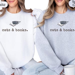 K&ouml;nnte beinhalten: Wei&szlig;e und graue Sweatshirts mit dem Text "cats & books". Jedes Sweatshirt hat eine kleine Grafik einer Katze auf einem Buch. Die Sweatshirts sind ein bequemer, l&auml;ssiger Stil.