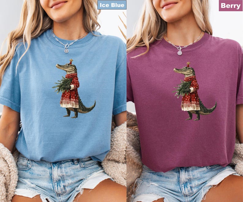 Pu&ograve; includere: T-shirt blu ghiaccio e color bacca con un'illustrazione stravagante di un alligatore vestito con un cappotto rosso con finiture bianche e un cappello festivo, che tiene un piccolo albero di Natale. L'alligatore &egrave; l'elemento centrale del design.