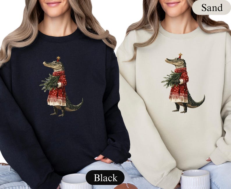 Pu&ograve; includere: Felpe nere e color sabbia con un'illustrazione stravagante di un alligatore vestito con un abito rosso festivo, che tiene in mano un fascio di rami sempreverdi. L'alligatore indossa un cappello a stella, aggiungendo un tocco festoso al design.