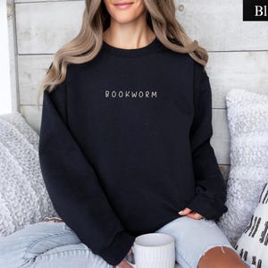 May include: Black crewneck sweatshirt with the word "BOOKWORM" embroidered in white. The sweatshirt is a solid black color and is made of a soft material. The sweatshirt is a casual style and is perfect for book lovers.