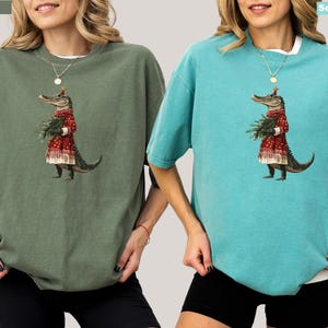 Pu&ograve; includere: Due magliette oversize, una verde muschio e una blu acqua marina, con un'illustrazione stravagante. La grafica raffigura un alligatore con un cappotto rosso fantasia e che tiene del verde. Le magliette hanno maniche corte e una vestibilit&agrave; rilassata.