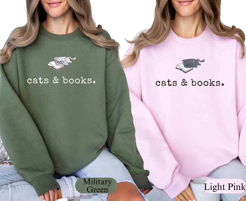 K&ouml;nnte beinhalten: Zwei Sweatshirts, eines in Milit&auml;rgr&uuml;n und eines in Hellrosa, jeweils mit einer Grafik einer Katze mit Brille auf einem Buch. Der Text "cats & books." ist darunter gedruckt. Die Sweatshirts sind lang&auml;rmlig.