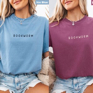 May include: Two short-sleeved t-shirts, one ice blue and one berry-colored. Each shirt has the word "BOOKWORM" printed in a contrasting color across the chest. The shirts are made of a soft material and are suitable for casual wear.