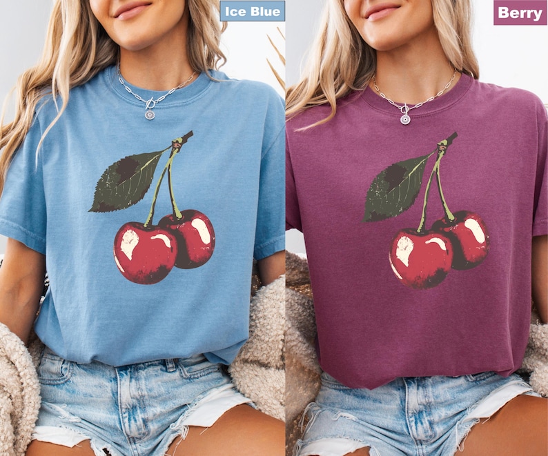 K&ouml;nnte beinhalten: Zwei kurz&auml;rmelige T-Shirts, eines in Eisblau und eines in Beere, jeweils mit einer Grafik von zwei roten Kirschen mit gr&uuml;nen Bl&auml;ttern. Die Shirts sind aus weichem Material und haben eine lockere Passform, geeignet f&uuml;r Freizeitkleidung.