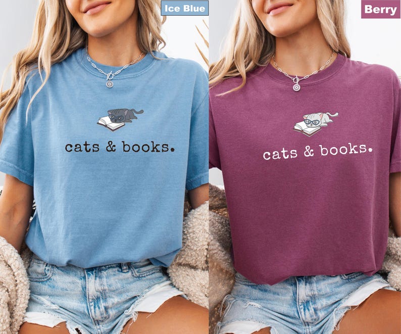 K&ouml;nnte beinhalten: Zwei kurz&auml;rmelige T-Shirts, eines in Eisblau und eines in Beere, jeweils mit dem Schriftzug "cats & books". Die Shirts zeigen eine Grafik einer Katze, die auf einem Buch liegt. Das eisblaue Shirt hat eine dunkelgraue Katze, w&auml;hrend das Beerenshirt eine Brille tragende Katze hat.