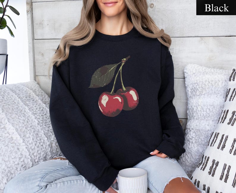 K&ouml;nnte beinhalten: Schwarzes Sweatshirt mit einer Grafik von zwei roten Kirschen und einem gr&uuml;nen Blatt. Die Kirschen haben einen Vintage-Look mit leichtem Used-Effekt. Das Sweatshirt ist einfarbig schwarz.