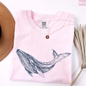 May include: A pink t-shirt with a black and white whale graphic. The shirt has the text "COMFORT COLORS" printed on the front.