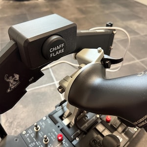 Könnte beinhalten: Ein schwarzes und silbernes Flugsimulator-Bedienfeld mit dem Text "CHAFF FLARE" auf einem Knopf. Das Panel enthält verschiedene Schalter, Knöpfe und einen Joystick. Das Design zeigt ein Logo und das Wort "OFF".