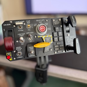 Puede incluir: Un panel de control negro con varios interruptores, botones y palancas. El panel tiene etiquetas como "JETT", "HOOK" y "EMERG BRK PULL". También se ven un botón rojo y una manija amarilla.