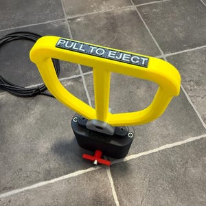 May include: A bright yellow handle with the text PULL TO EJECT in black letters, attached to a black base with a grey connector. A small red T-shaped lever is visible at the bottom of the black base, and a black coiled cable lies nearby.