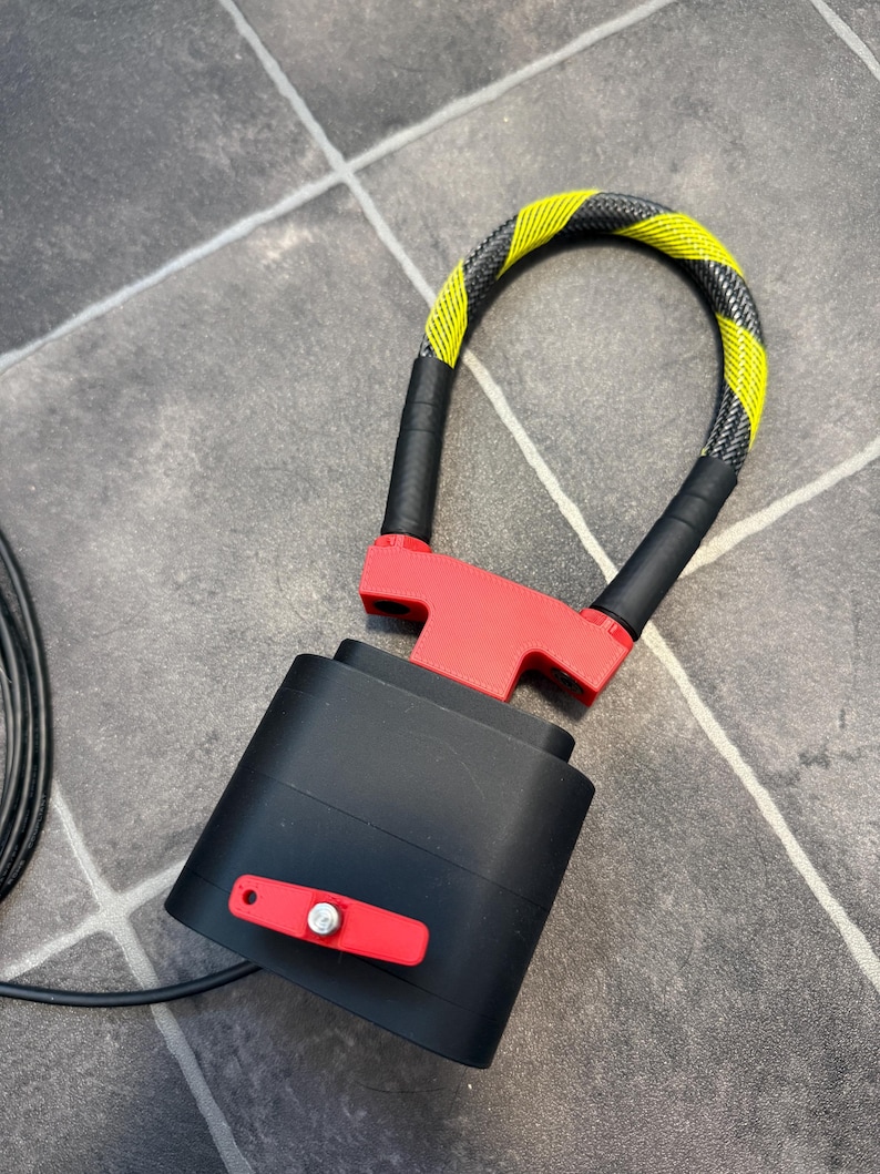 May include: A black and red security lock featuring a flexible cable with a yellow and black hazard pattern. The device includes a rectangular black housing with a red lever and a metallic silver pin, connected to a U-shaped locking mechanism.