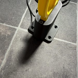 May include: A black 3D-printed mounting base with four circular screw holes, featuring a vertical yellow handle component inserted into the top. A thin black cable extends from the rear of the base, which has a textured, layered surface finish.