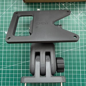May include: A black 3D-printed bracket with the text "PAP3" and a grey 3D-printed adjustable mount. The bracket has a rectangular opening and three screw holes. The mount has a knob for adjustment and metal pins.
