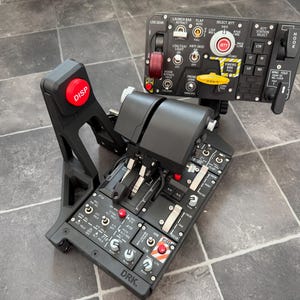Può includere: Un quadrante dell'acceleratore e pannello di controllo per simulatore di volo nero, dotato di numerosi interruttori, levette e pulsanti. L'unità include un pulsante rosso DISP, un pulsante JETT e varie etichette come LDG GEAR, HOOK e DRK.