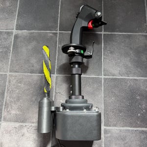 May include: A black flight simulator joystick featuring a contoured grip with a red trigger, multiple buttons, and a silver metal base. Attached to the side is a cylindrical component with a yellow and black striped protective cable sleeve.