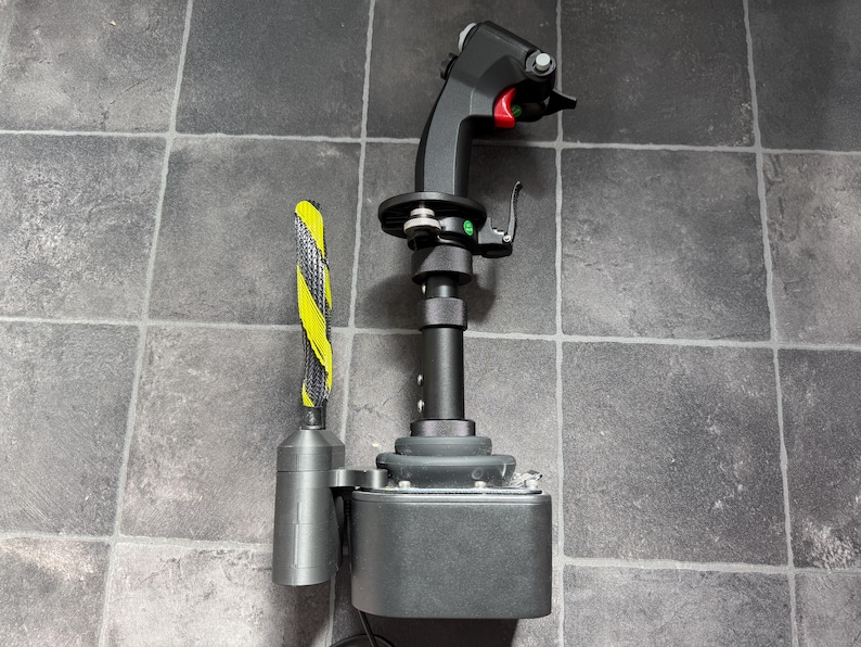May include: A black flight simulator joystick featuring a contoured grip with a red trigger, multiple buttons, and a silver metal base. Attached to the side is a cylindrical component with a yellow and black striped protective cable sleeve.