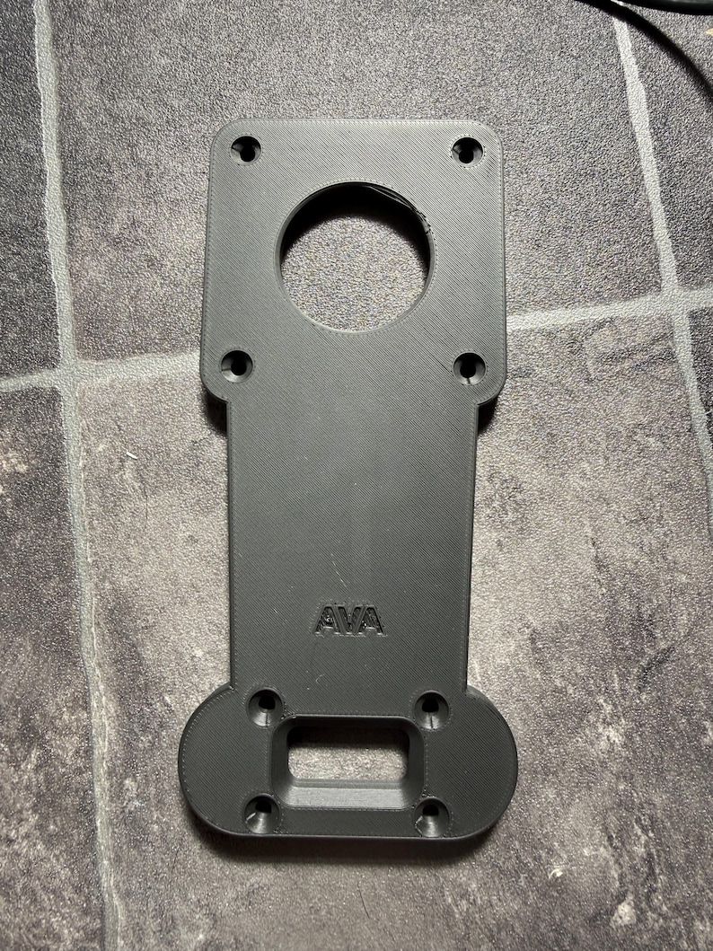 May include: A matte black, 3D-printed mounting plate with a rectangular top section featuring four circular screw holes and a large central circular cutout. The lower section has four smaller screw holes and a rectangular cutout, with the text AVA embossed.