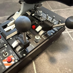 以下が含まれることがあります： さまざまなスイッチ、ノブ、レバーを備えた黒いフライトシミュレーターのコントロールパネル。パネルには、「A/G」、「A/A」、「DECR」、「INCR」、「ENG」、「DIS」、「A10」、「PATH」、「ALT/HDG」、「OFF」、「ALT」、「HDG」、「CRS」、「PANEL LTS」、「SIM」、「ARM」、「RE ARM」、「MS」、「TE」、「PITON」、「ALT HOLD」、「F16」、「G」、「PUSH」などのラベルがあります。