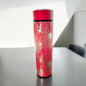 May include: A red insulated water bottle with a gold spiderweb and spider design.