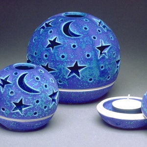 Könnte beinhalten: Drei blaue Kerzenhalter aus Keramik mit einem Mond- und Sternenmuster. Die Halter sind in verschiedenen Größen und aus einem gesprenkelten blauen Glasur.