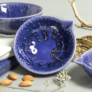 May include: A set of four blue ceramic bowls with a white crackle glaze. The bowls are handmade and have a unique, rustic look.