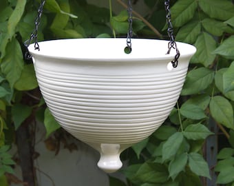 May include: White ceramic hanging planter with a ribbed design and a rounded bottom. The planter is suspended by a black chain.