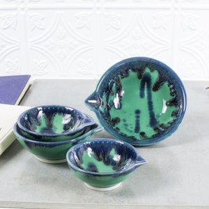 Op de afbeelding: Set van vier groene en blauwe keramische kommen met een gespikkeld glazuur. De kommen zijn in elkaar genest en hebben een giettuit.