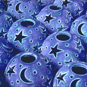 May include: A collection of blue ceramic candle holders with cut-out stars and crescent moons. The holders have a speckled blue glaze.