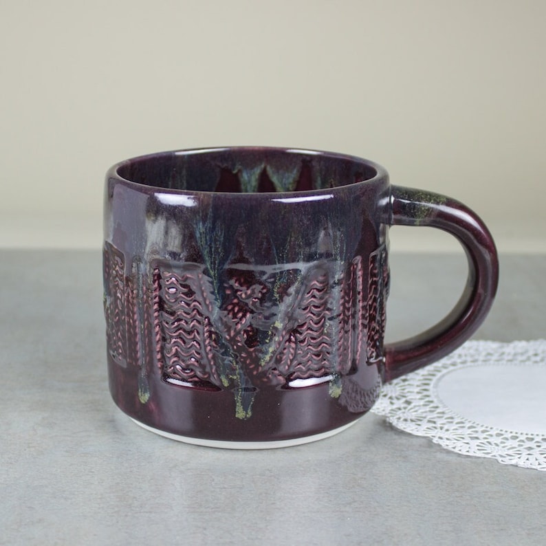 May include: A handcrafted ceramic mug with a deep purple glaze and textured design. The mug features a unique pattern and a comfortable handle. The interior is a lighter shade of purple. A decorative piece for coffee or tea.