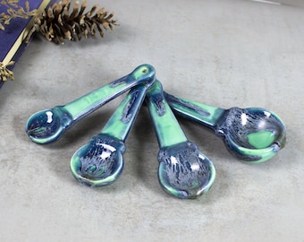 May include: Set of four ceramic measuring spoons in a blue and green glaze. The spoons are arranged in a fan shape.