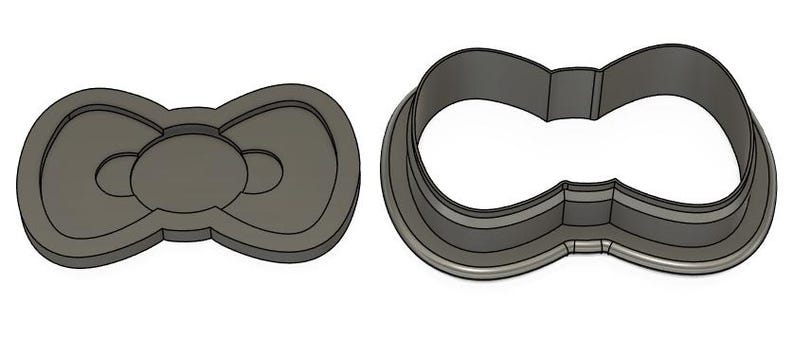 May include: A metal cookie cutter shaped like a bow. The cutter has a detailed design with a center circle and two loops.