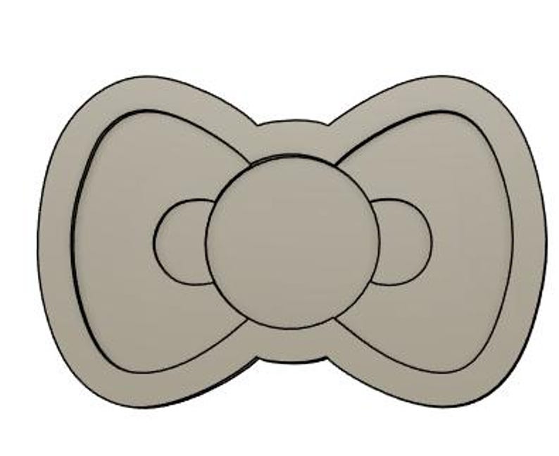 May include: A gray bow-shaped cookie cutter with a circle in the center and two smaller circles on each side.