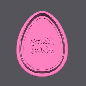 May include: A pink, egg-shaped object with a raised border and the cursive text "Sarah's Garden" engraved on the surface. The object is set against a grey background.