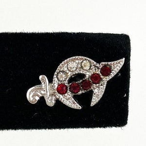 May include: A silver crescent moon and sword pin with red and clear rhinestones.