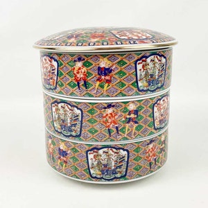 May include: A three-tiered porcelain serving dish with a lid. The dish is decorated with a colorful pattern of ships, people, and geometric designs.