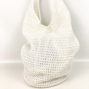 May include: White crochet tote bag with a slouchy, unstructured design. The bag is made of a fine, open weave and has a single strap.