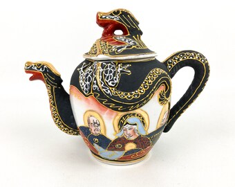 Könnte beinhalten: Dekorative Keramik-Teekanne mit Drachendesign. Die Teekanne hat einen schwarzen Körper mit goldenen Akzenten, einen roten Drachenausguss und -griff sowie einen Deckel mit einem Drachenkopf. Der Körper der Teekanne zeigt eine bemalte Szene mit Figuren.