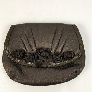 May include: A brown leather clutch purse with a decorative row of fabric roses across the front.