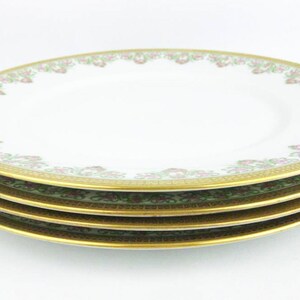 May include: A stack of four white porcelain plates with a gold rim and a floral design in pink and green. The plates are stacked on top of each other, showcasing the intricate details of the design.