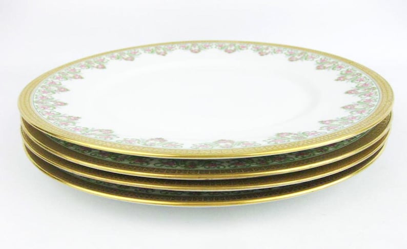 May include: A stack of four white porcelain plates with a gold rim and a floral design in pink and green. The plates are stacked on top of each other, showcasing the intricate details of the design.
