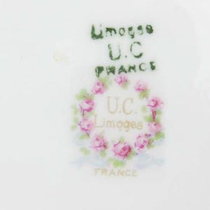 May include: Close-up of a white porcelain surface with the text "Limoges U.C. France" in green and gold. A wreath of pink roses encircles the letters "U.C. Limoges France".