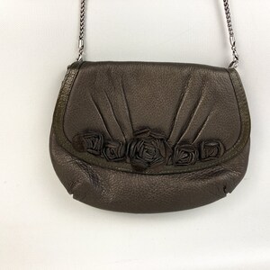 May include: A brown leather crossbody bag with a silver chain strap and a floral design on the front flap.