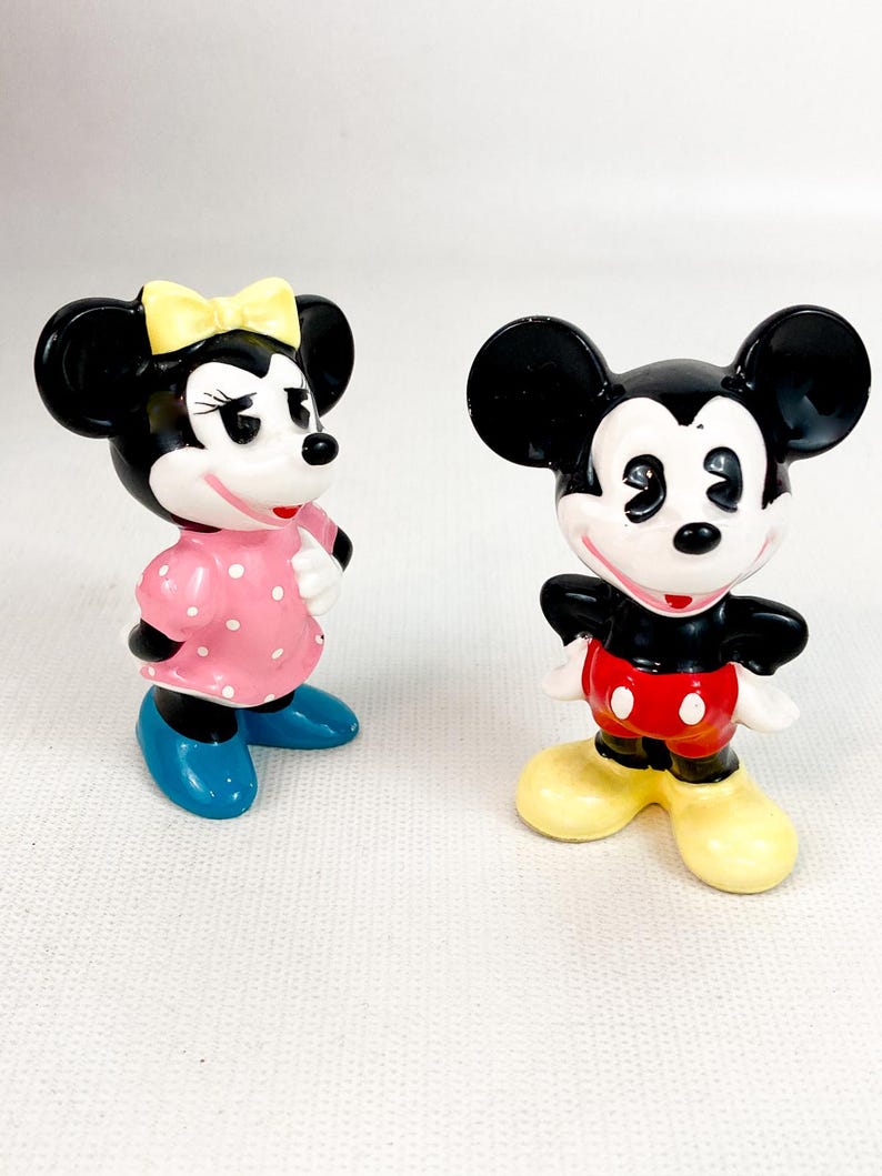 Może przedstawiać: Dwie figurki postaci z kresk&oacute;wek Myszki Miki i Myszki Minnie. Myszka Minnie ma na sobie r&oacute;żową sukienkę w kropki, niebieskie buty i ż&oacute;łtą kokardę. Myszka Miki ma na sobie czerwone szorty, ż&oacute;łte buty i czarny top.