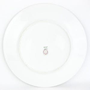 May include: White ceramic plate with a wide rim. The underside features a small, circular emblem with floral details and the text "Limoges France". The plate is round and appears to be a dinner plate.