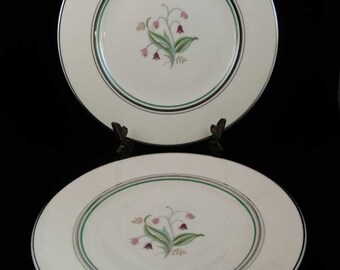 May include: Two white ceramic dinner plates with a green and black trim. The center of each plate features a floral design with pink and purple flowers.